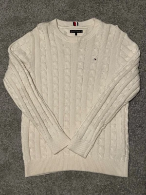 Vit kabelstickad tröja Tommy Hilfiger - Säljer en vit kabelstickad tröja från Tommy Hilfiger i storlek 164 men passar även upp mot 175. Säljer den eftersom den varit oanvänd sedan januari förra året vilket ger den ett  suveränt skick på ungefär 9/10.                                                          En väldigt stilren tröja som även är lite tjockare vilket gör den perfekt till höst/vinter. Hör av er vid några som helst frågor😁