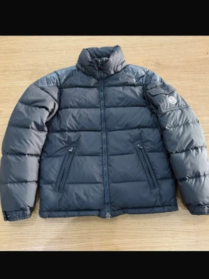 Moncler svart dunjacka – klassisk & varm, fint skick - Säljer en äkta svart Moncler dunjacka i klassisk design.  🧥 Färg: Svart 📏 Storlek: 14 y( fits 1 sized)  🔎 Skick: Fint / mycket bra skick (se bilder)  Jackan är varm och stilren, perfekt nu på vintern. Hör av dig om du vill se närbilder på patch, dragkedja eller foder! 