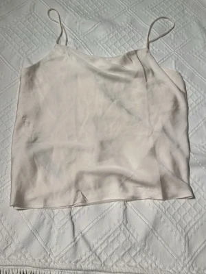 Ljusbeige linnetopp från Mango - Säljer en stilren ljusbeige linnetopp från Mango med tunna axelband och slät, mjuk yta. Toppen har en enkel och rak passform som är perfekt för varma dagar. Materialet känns lent och har en lätt glansig finish.