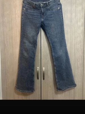 Blå bootcut jeans från H&M Divided - Säljer ett par blå bootcut jeans från H&M Divided i storlek 40. Jeansen har klassisk femficksdesign, normal passform och är tillverkade i jeansmaterial med snygg tvätt. Perfekt för dig som gillar retrovibbar och vill ha ett par jeans med lite vidare ben.