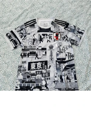 Japan Tokyo printad t-shirt Adidas - Säljer en svartvit t-shirt från Adidas med coolt Tokyo-inspirerat grafiskt tryck över hela plagget. Kortärmad modell med klassiska Adidas-ränder på axlarna och JFA-logga på bröstet. Materialet känns som mjuk polyester, perfekt för dig som gillar streetstyle och unika prints.