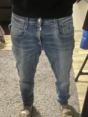 Replay anbass - Storlek W29 L30 Säljer ett par snygga blå jeans från Replay med klassisk femficksdesign och coola detaljer på bakfickorna. Jeansen har tapered passform, dragkedja och knapp i midjan. Materialet är slitstarkt jeans och färgen är ljusblå med tvättade effekter.