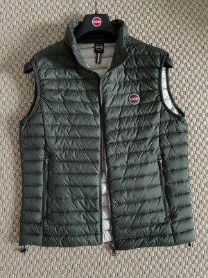 Mörkgrön dunväst från Colmar - Säljer en mörkgrön dunväst från Colmar med quiltad design och hög krage. Västen har två praktiska fickor med dragkedja och Colmar-logga på bröstet. Perfekt att slänga på sig när det är kyligt ute. Stängs med dragkedja framtill.