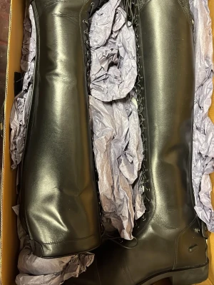 Svarta höga ridstövlar i skinn, strl 39 - Säljer ett par helt nya svarta höga ridstövlar med snörning hela vägen upp och rund tå. Stövlarna  har en snygg, stilren look med detaljer i svart. Passar vadstorlek 35-40 cm och har en höjd på 50 cm.