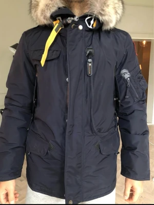 Mörkblå Parajumpers parkajacka med päls - Parajumper Right Hand Light HELT NY  Hej! Säljer min Parajumper Vinterjacka då jag inte använder den & den tar onödig plats. Jackan har kod så man kan se så att den är äkta! Kan gå ner i pris men då ska det vara seriös affär & inga skambud!!!  Kön: Herr Passform: Normal Material Yttertyg: 100% Polyster Material Fyllning: 90% Dun Pälsen är äkta tvättbjörn & inre päls är bäver! Tvättråd: Kemtvätt (Aldrig tvättad då den är ny) Färd: Marinblå Säsong: Höst/Vinter Varumärke: Parajumper