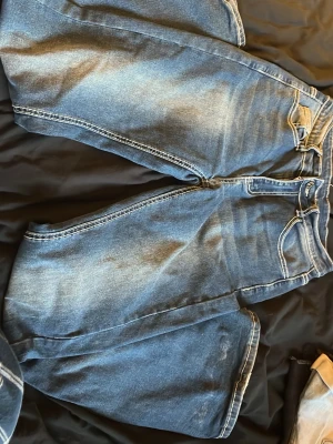 Blå jeans med korsdetalj  - Säljer ett par blå jeans från Romwe/SHEIN i storlek S. Byxorna har en snygg broderad korsdetalj på bakfickorna och kontrastsömmar. Klassisk femficksmodell med knapp och dragkedja. Perfekta för dig som vill sticka ut lite extra.