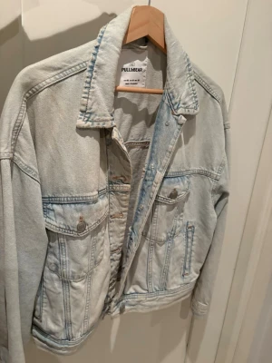 Ljusblå jeansjacka från Pull&Bear - Säljer en klassisk ljusblå jeansjacka från Pull&Bear i storlek M. Jackan har två bröstfickor med knappar, sidofickor och en rak passform. Den är aldrig använd.