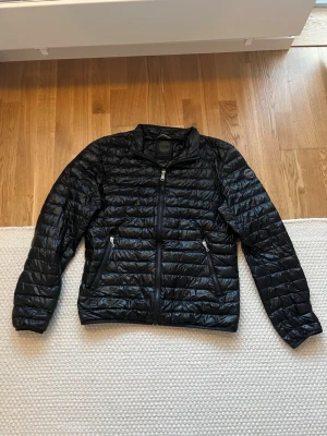 Svart pufferjacka från Colmar - Säljer en svart pufferjacka från Colmar Originals i storlek 50. Jackan har quiltad design, två dragkedjeförsedda fickor och Colmar-logga på ärmen. Tillverkad i glansig polyester och perfekt för kyliga dagar. Stängs med dragkedja framtill. PRISET ÄR FAST