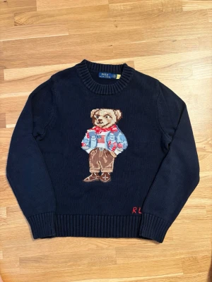 Polo Ralph Lauren bear sweatshirt - Mörkblå stickad tröja från Polo Ralph Lauren med ikonisk björn broderad på bröstet. Sparsamt använd så skicket är som ny. Passar längd 160-165 cm, dvs S storlek. 