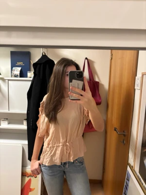 Beige blus med knyt från Twinset - Supersöt beige blus från Twinset Milano med korta ärmar, volangdetaljer och knyt i midjan. Blusen har en avslappnad passform och är gjord i ett tunt, mjukt material som känns luftigt. 