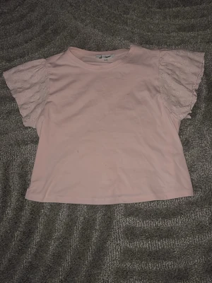 Ljusrosa blus med spetsärmar - Supersöt ljusrosa blus från Cubus i storlek 134. Toppen har korta, vida ärmar i spets med broderade detaljer som ger en romantisk vibe. Själva kroppen är i mjuk bomull och har en enkel, rak passform. Perfekt för dig som gillar gulliga och feminina plagg.