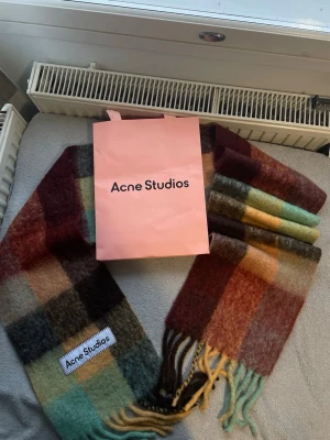 Rutig Acne Studios ullhalsduk - Säljer en sjukt snygg rutig halsduk från Acne Studios i mjuk ull. Färgerna går i grönt, brunt, beige, gult och vinrött. Stor Acne Studios-logga och långa fransar i ändarna. Perfekt accessoar för att lyfta din outfit.