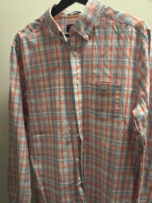 Rutig skjorta från Gant i bomull - Säljer en rutig skjorta från Gant i mjuk bomull. Skjortan har en klassisk krage, knappstängning framtill och en bröstficka med broderad Gant-logga. Färgerna är en mix av rött, blått och vitt. 