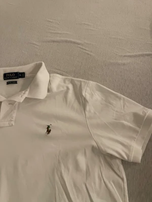 Vit pikétröja från Polo Ralph Lauren XL - Klassisk vit pikétröja från Polo Ralph Lauren i storlek XL. Tröjan har korta ärmar, krage och knappslå framtill samt den ikoniska broderade loggan på bröstet. Tillverkad i mjuk bomull för en skön känsla.