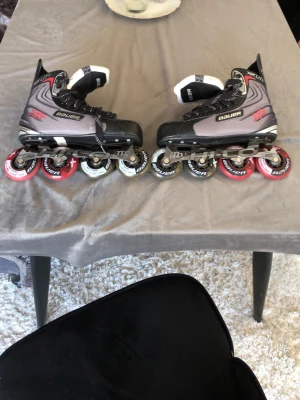 Bauer Vapor XR Lite inlines - Säljer ett par Bauer Vapor XR Lite inlines med svart och grå ovandel, röda och vita hjul samt svarta snören med vita detaljer. Skorna har robust design och är perfekta för dig som vill åka snabbt och smidigt. Märket syns tydligt på sidan och plösen.