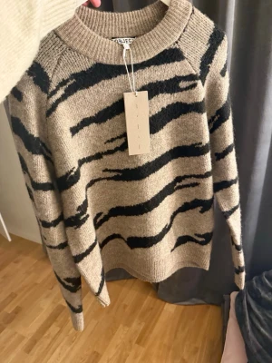 Beige zebramönstrad stickad tröja Object - Säljer en beige stickad tröja från Object i storlek S med svart zebramönster. Tröjan har rund halsringning, ribbade muddar och lång ärm. Perfekt för dig som vill ha en trendig och mysig look till hösten och vintern.