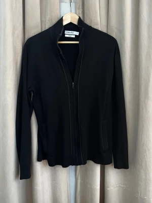 Svart kofta från Calvin Klein - Svart zip-tröja från Calvin Klein. Funkar året runt, lätt att slänga över en t-shirt eller skjorta. Skön passform och smidig dragkedja hela vägen upp.  Använd men i bra skick, inget som sticker ut. Perfekt att ha till vardags eller vid lite mer uppklädda tillfällen. Tröjan är i storlek M men jag skulle säga att den passar mer som en S.                                                                       Hör av dig om du vill ha mer bilder eller mått😁