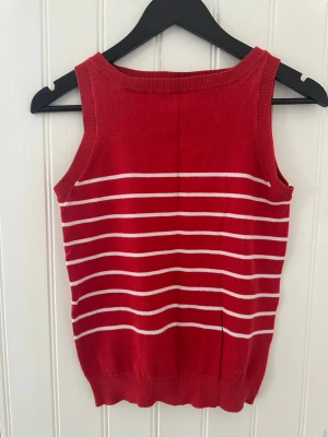 Röd randig linnetopp från Zara - Säljer en röd ärmlös linnetopp från Zara med vita horisontella ränder. Toppen har rund halsringning och är gjord i mjuk bomullsblandning med 70% bomull och 30% nylon. Perfekt för varma dagar och enkel att styla till jeans eller kjol.
