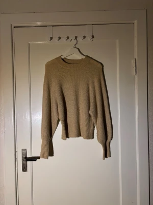 Beige ribbad stickad tröja - Mysig beige stickad tröja med ribbad struktur och rund hals. Tröjan har långa ärmar och en något loose passform som ger en avslappnad vibe. Perfekt att slänga på sig under kyliga dagar.