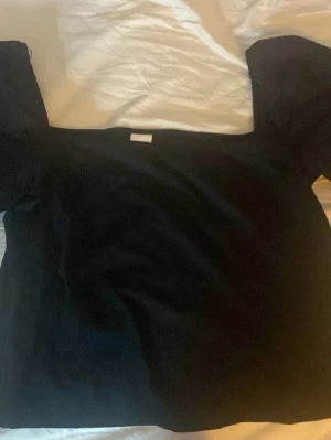 Svart offshoulder topp från H&M - Säljer en svart offshoulder topp från H&M i storlek XL. Toppen har en rak, croppad passform och ärmlös design med breda axelband som sitter nedanför axlarna. Perfekt att styla med höga jeans eller kjol.