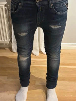 Replay jeans blå, W28 L30 - Säljer ett par mörkblå   jeans från Replay med slitna detaljer och snygga sömmar på bakfickorna. Jeansen har klassisk femficksdesign, låg midja och är tillverkade i stretchigt denim för en tight passform. Perfekta för dig som gillar en modern och smal siluett.
