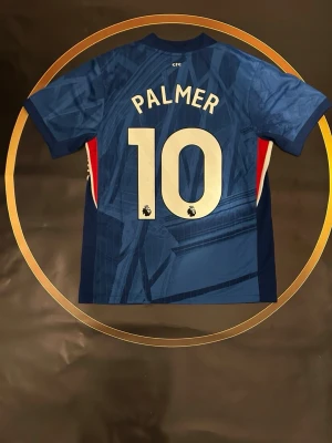 Chelsea Nike matchtröja Palmer #10 - Chelsea FC matchtröja från Nike i marinblått med grafiskt mönster, Palmer och nummer 10 på ryggen. Tröjan har klubbmärke och Nike-logga på bröstet samt röda och vita detaljer vid sidorna. Tillverkad i lätt polyester med Dri-FIT-teknologi.