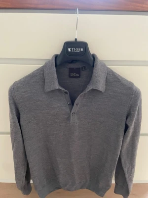 Grå pikétröja i ull från Oscar Jacobson - Snygg grå långärmad pikétröja från Oscar Jacobson, tillverkad i Italien. Tröjan är i mjuk ull med klassisk krage och knappar framtill. Perfekt för dig som gillar stilrena och tidlösa plagg. Tröjan är liten i storleken så passar xs/s. Hör av er vid frågor