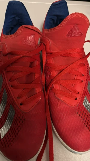 Röda adidas fotbollsskor med snörning - Säljer ett par röda adidas fotbollsskor för inomhus. Med klassiska silverfärgade ränder på sidorna. Storlek FR 36, UK 3 1/2