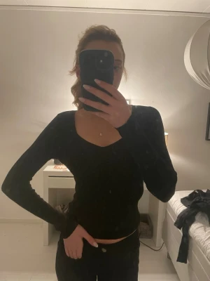 Svart långärmad topp med v-ringning - En stilren svart långärmad topp med v-ringad hals. Sitter tight och har en enkel, klassisk design som passar till många olika outfits. Perfekt för dig som gillar en clean och tidlös look.