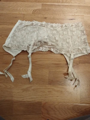 Strumpebandshållare - Säljer en romantisk vit strumpebandshållare med fin spets från Ella May, exklusiv för Lindex. Den har har broderade blommor, genomskinliga spetsdetaljer och fina band för på fästena. Perfekt som present på alla hjärtans dag / Valentine's day. Jag har fler annonser uppe så titta gärna på min sida!