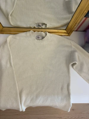 Vit tröja -  vit ribbad stickad tröja från ONLY. Tröjan har lång ärm, hög hals och är i mjukt material som passar perfekt till kyligare dagar. Enkel och clean look som är lätt att styla med allt.