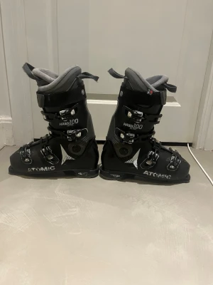  pjäxor Atomic Hawx Ultra 100 - Säljer ett par svarta Atomic Hawx Ultra 100 pjäxor med fyra metallspännen och grå vadderad insida. Snygg design med vita detaljer och logga på sidan. Priset kan förhandlas vid snabb affär.