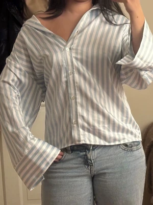 Randig skjorta - Säljer en snygg skjorta från Gina Tricot i storlek S. Skjortan har ljusblå och vita vertikala ränder, breda manschetter och knappar framtill. Modellen är loose fit med klassisk krage och lång ärm. Perfekt att styla med jeans eller kjol.