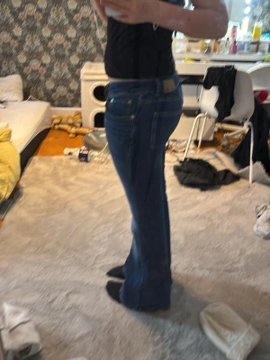 Blå bootcut jeans från 151® - Säljer ett par blå jeans från lager175® i storlek M med kort benlängd. Modellen har låg midja och klassisk bootcut-snitt som ger en snygg siluett. Jeansen har fem fickor, dragkedja och knapp framtill. Perfekt för dig som gillar retrovibe och bekväma jeans.