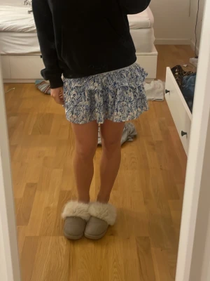 Blommig kortkjol från Gina Tricot - Supersöt kortkjol från Gina Tricot med blått och vitt blommönster. Kjolen har volangkant och smock i midjan för en bekväm och snygg passform. Perfekt för dig som gillar en fräsch och somrig stil!