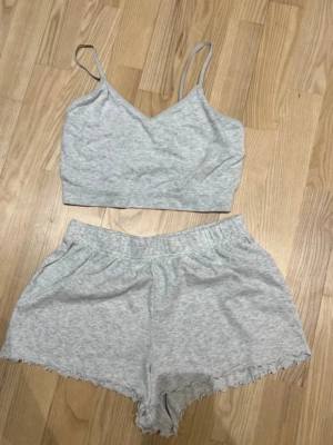 Pyjamasset - Säljer en ljusgrå croppad linnetopp med smala axelband och v-ringad hals. Toppen är i mjuk bomull och har en enkel, stilren look som passar perfekt till sommaren. Matcha med shorts eller kjol för en chill vibe.