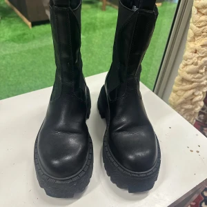 Svarta chunky boots från Steve Madden 37 - Svarta boots från Steve Madden med grov sula och högt skaft. Skorna är tillverkade i skinn med textildetaljer på sidorna och har en rejäl plattform. Perfekta för dig som gillar en edgy och trendig stil.
