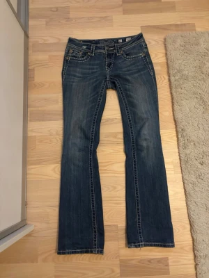 Miss Me jeans med broderade bakfickor - Snygga blå jeans från Miss Me med unika broderade bakfickor med pärldetaljer och blommotiv. Jeansen har låg midja, bootcut model och klassisk femficksdesign. Säljer dessa jeans pågrund av att de är för stora. Lite slitna längst ner på jeansen men i övrigt bra skick. Köpta för 1500kr.