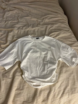 Vit oversized t-shirt från Gina Tricot - Den är inte använd nån gång, köpte men har inte använt den än. En basic vit t-shirt från Gina Tricot i oversized modell. Tillverkad i mjuk bomull med rund halsringning och korta ärmar. Perfekt att styla med jeans eller kjol för en clean och enkel look.