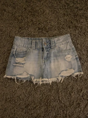 Ljusblå jeanskjol med slitningar - Kort lågmidjad jeanskjol i ljusblå denim med slitna detaljer och fransig nederkant. Använd vid 3 tillfällen.