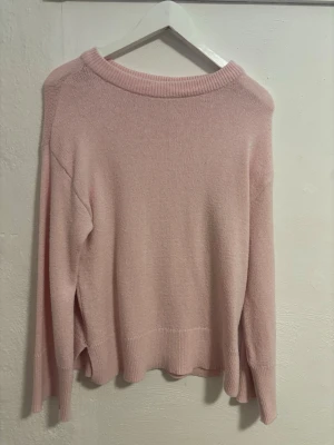 Ljusrosa stickad tröja från 157 - Supersöt ljusrosa stickad tröja från 157 i storlek XS. Tröjan har lång ärm, ribbade muddar och en liten slits på slutet av tröjan för extra detalj. Perfekt för lager på lager under höst och vinter.