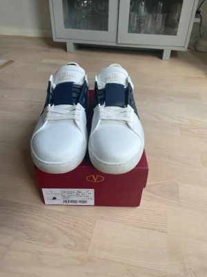Valentino Garavani One Stud sneakers - Säljer ett par vita Valentino Garavani Open. Snygga skor med snygg marin blå detalj. Lådan och valentino påsen ingår.