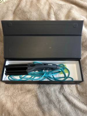 Lyko vågtång för hårstyling - Säljer en svart vågtång från Lyko med turkos sladd. Perfekt för att skapa snygga beach waves. Ergonomiskt handtag med on/off-knapp och låsfunktion. Kommer i stilren svart box. Material: plast och metall.