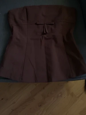 ...Brun axelbandslös tubtopp med rosett🫶🏼 - Super fin brun axelbands lex tubtopp med en liten söt rosettdetalj framtill. Toppen har en lätt utsvängd passform och är sydd i  stretchigt tyg. Perfekt för dig som vill ha en enkel men ändå chic look.