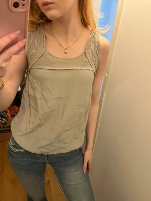 Beige linnetopp från Banana Republic - Säljer en stilren beige linnetopp från Banana Republic i storlek XS Petite. Toppen har breda axelband med snygga sydda detaljer och är tillverkad i ett tunt, lätt material som känns luftigt. 