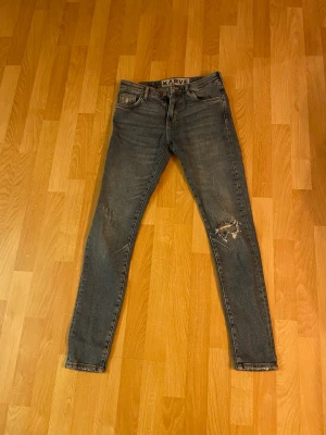 Grå skinny jeans från Karve - Säljer ett par gråa skinny jeans från Karve med slitningar på ena benet och bakfickorna. Klassisk femficksmodell med dragkedja och knapp. Jeansen har en smal passform och är tillverkade i jeansmaterial.158-164