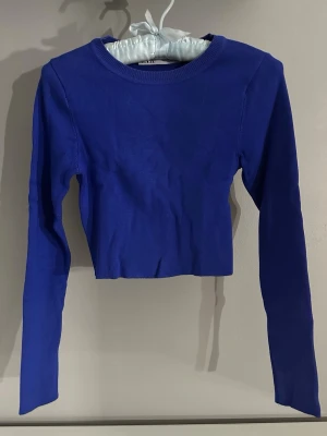 Blå croppad långärmad topp - Snygg blå croppad topp från Zara med lång ärm och rund halsringning. Enkel och stilren design som passar perfekt till jeans eller kjol. Tillverkad i mjukt material för en bekväm känsla.
