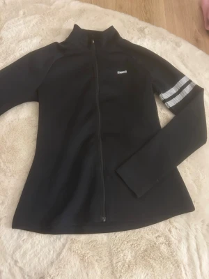 Svart zipjacka från Stronger - En figursydd träningsjacka från stronger, helt oanvänd i storlek M, jag är vanligtvis en S och den sitter toppen på mig också men om man vill ha den rätt så tajt så är den perfekt!