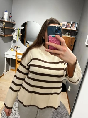 Beige brun randig tjock stickad tröja Vero Moda - Jättefin beige brun stickad tröja från Vero Moda i storlek M. Den har en liten fläck på ärmen på baksidan som knapp syns. Den är perfekt nu i det kalla vädret men funkar såklart också när som helst. Den är luftig längst ner på tröjan samt att den går lite nedanför rumpan men inte så att den sitter fast när man sitter ned