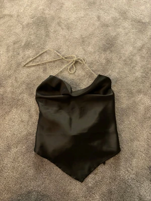 Svart satin halternecktopp från Gina Tricot - Säljer en svart halternecktopp från Gina Tricot i satin. Toppen har smala glittriga band att knyta i nacken och en snygg knytning i ryggen. I strl S men passar även XS, den är endast använd en gång💞💞
